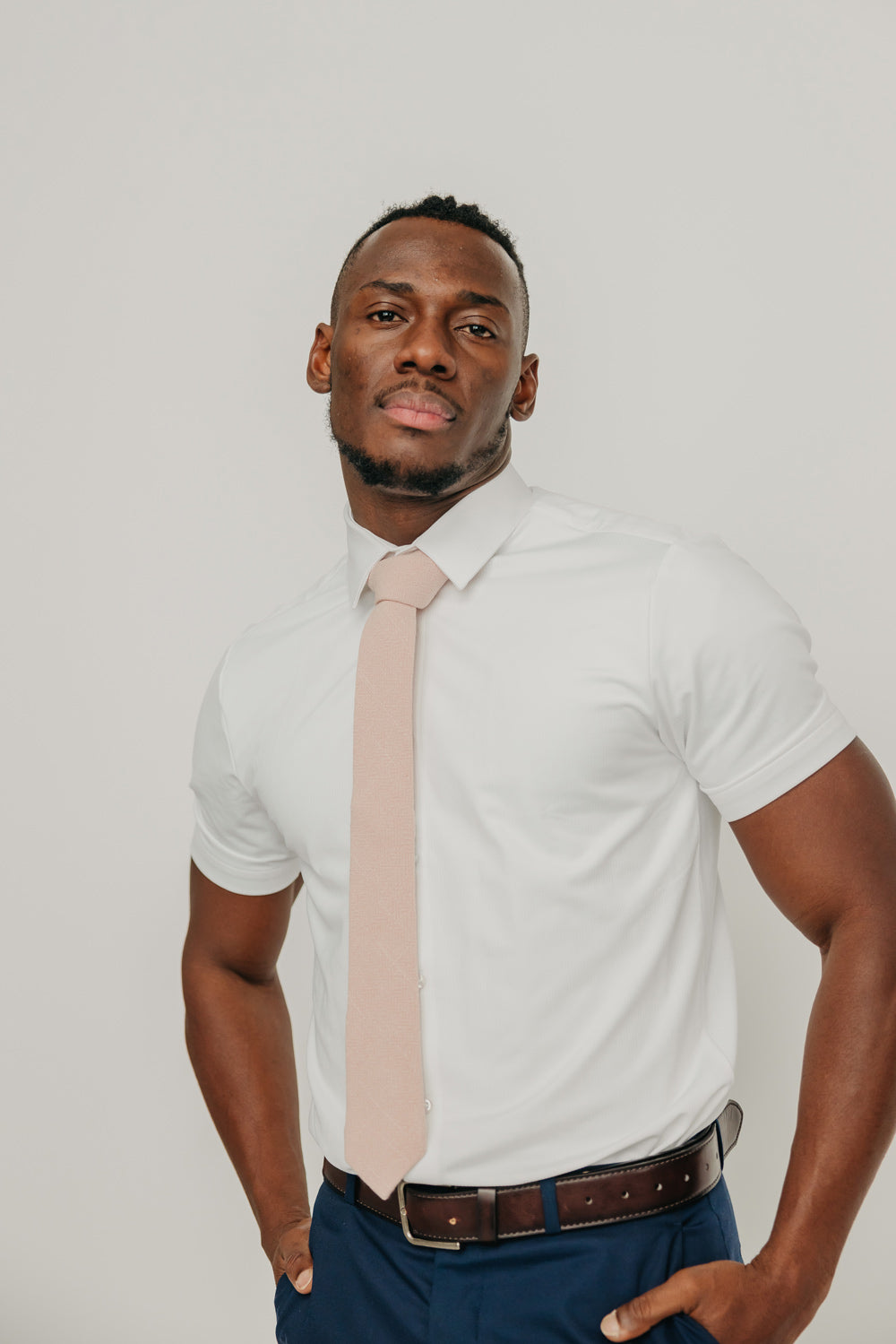 Mauve tie worn with a white shirt, brown belt and blue pants.