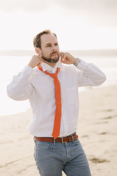 Tangerine tie worn with a white shirt and blue pants.