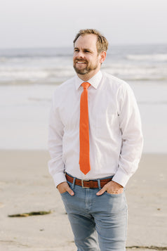 Tangerine tie worn with a white shirt and blue pants.