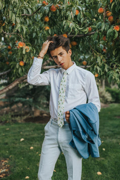 Desert Sun tie worn with white shirt and light gray pants. Model is also holding a blue suit jacket.