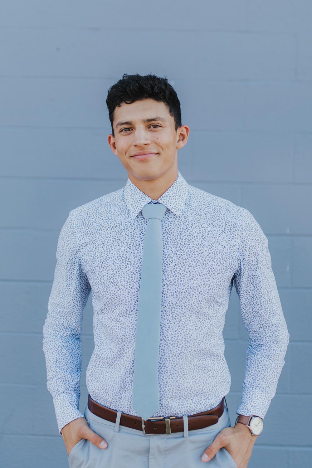 Dusty tie worn with a blue patterned shirt, brown belt and light gray pants.