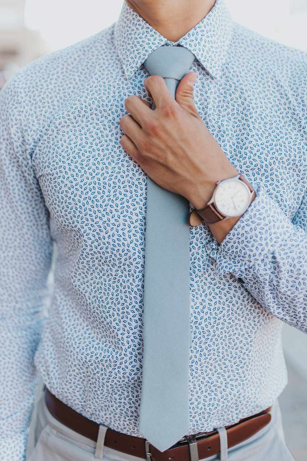 Dusty tie worn with a blue patterned shirt, brown belt and light gray pants.