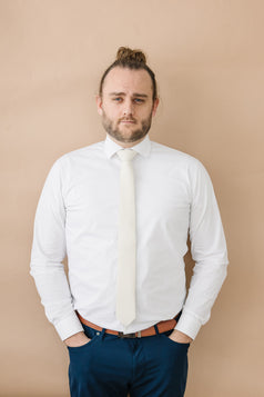 Ivory tie worn with a white shirt, brown belt and navy blue pants.