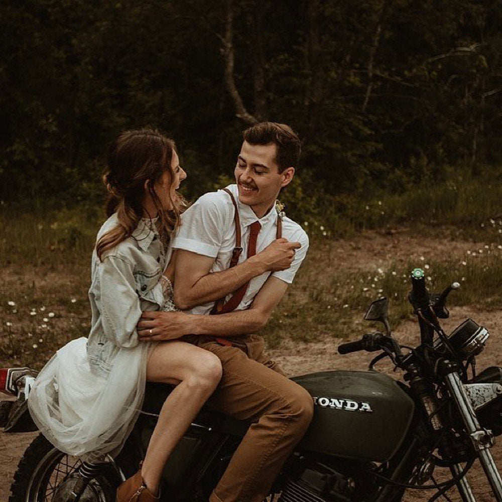 Rust tie worn with a white shirt and brown leather suspenders, sitting on a motorcycle.